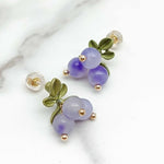 Pair of earrings with purple beads and green leaves on a marble surface