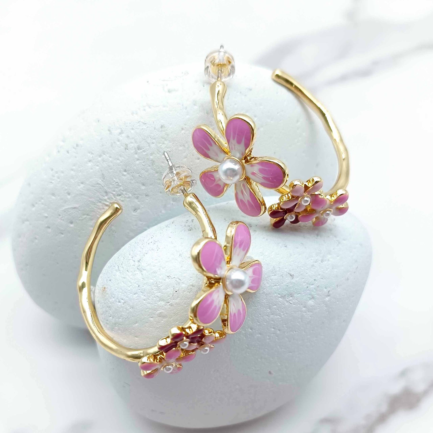 Gold hoop earrings with pink floral designs on a white background