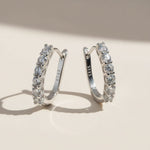 Pair of silver hoop earrings with clear lab-grown diamonds on a beige background