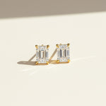 Emerald-cut moissanite stud earrings in platinum plated silver on neutral background.