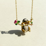 Gold chain necklace featuring a hand-painted enamel sloth pendant hanging from a floral branch with pink flowers and green leaves