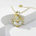 Gold and white teapot-shaped pendant on a chain against a white background