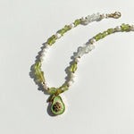 Necklace with green teardrop pendant and white beads on a light background