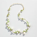 Necklace with white beads and green floral elements on a light gray background