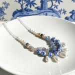 Handcrafted necklace with blue ceramic beads, freshwater pearls, and tanzanite stones on white plate.