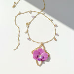 Gold necklace with a pink flower pendant on a white background