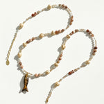 Long gemstone and ceramic bead necklace with carved fish pendant laid out in sunlight