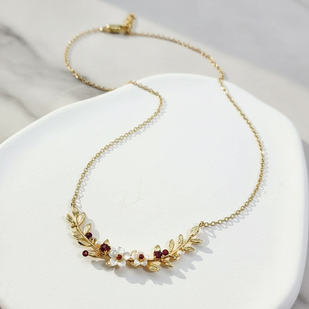 Gold necklace with leaf and berry design on a white surface