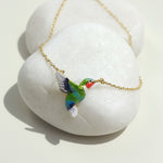 Colorful bird-shaped pendant on a gold chain against a white stone background
