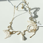 Delicate gold necklace with leaf designs and pearls on a white background