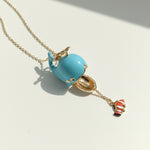 Necklace with a turquoise whale pendant and gold chain on a light background