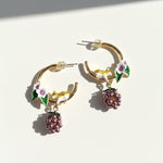 Gold hoop earrings with floral and berry charms on a white background