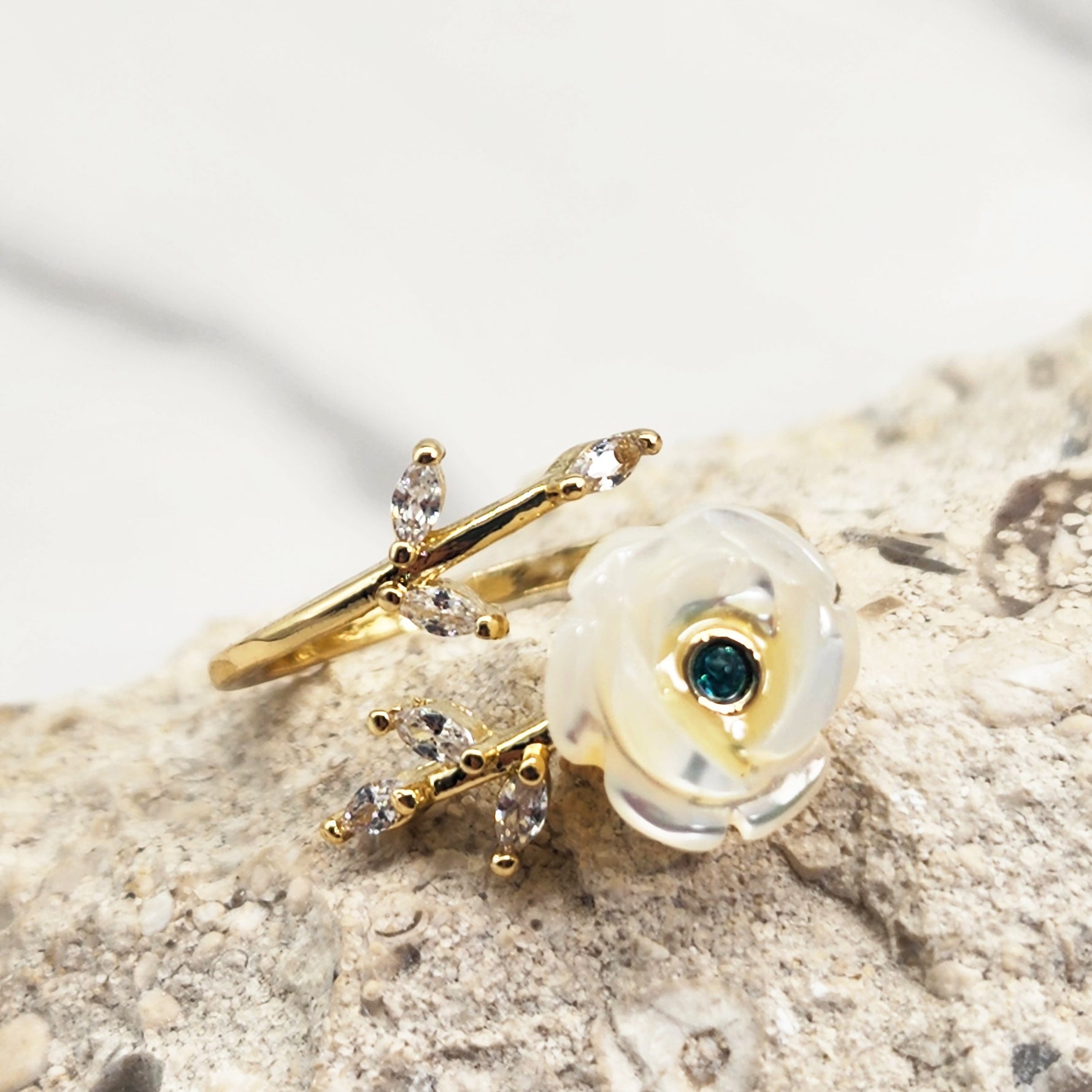 Adjustable gold-plated ring featuring a hand-carved mother-of-pearl flower and cubic zirconia leaves, displayed on a natural stone background.