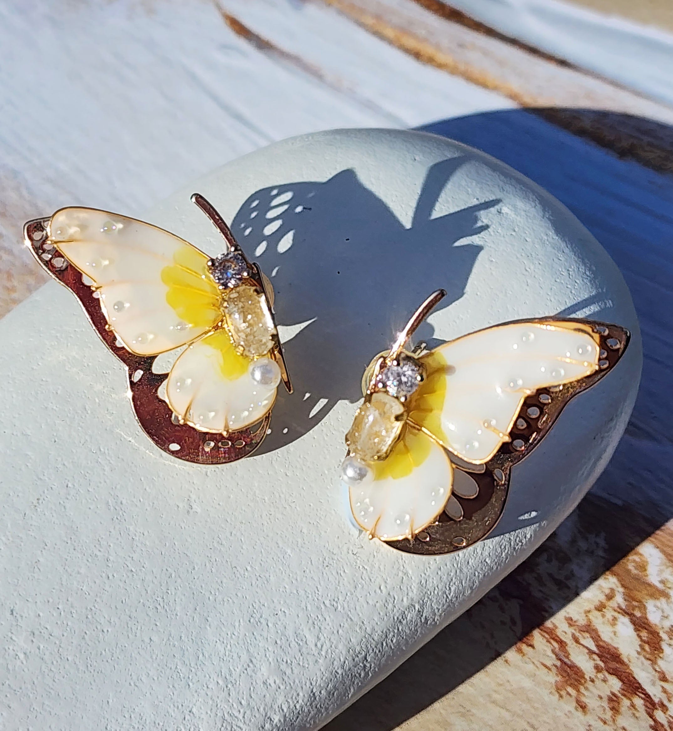 Handpainted butterfly stud earrings with various birthstone-colored resin wings, gold-plated brass, and 12 months' birthstone cubic zirconia center stones, displayed in natural sunlight