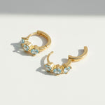 Gold-plated silver hoop earrings with three light blue cubic zirconia birthstones, elegant minimalist design.