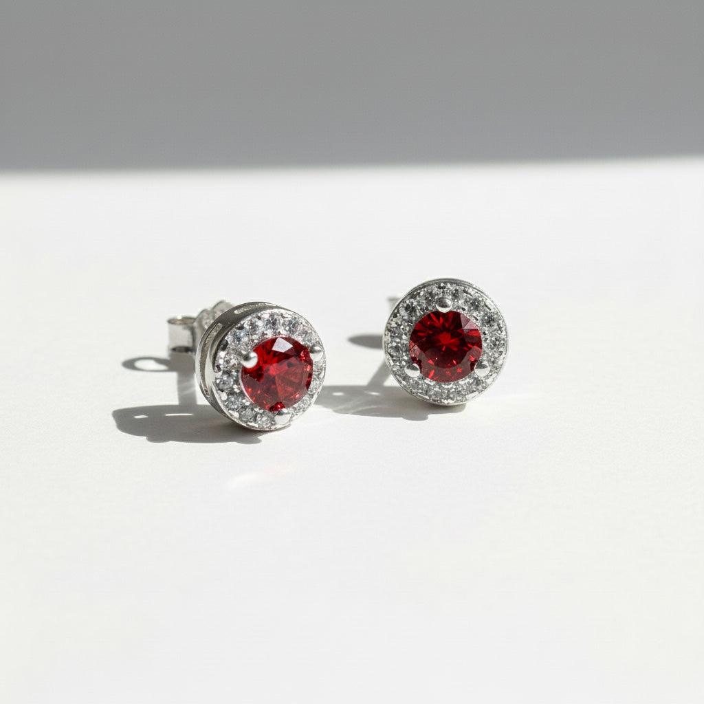 Silver stud earrings with platinum plating and garnet birthstone center, surrounded by clear CZ halo.
