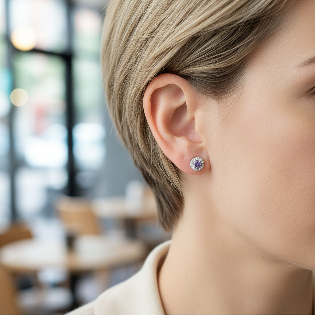Model wearing silver stud earrings with platinum plating and purple birthstone center surrounded by CZ halo.