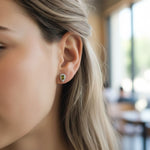 Model wearing teardrop green birthstone stud earrings with platinum-plated silver setting and halo of clear CZ stones.