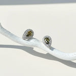 Teardrop stud earrings with olive green birthstone, platinum-plated silver setting, and halo of clear cubic zirconia.