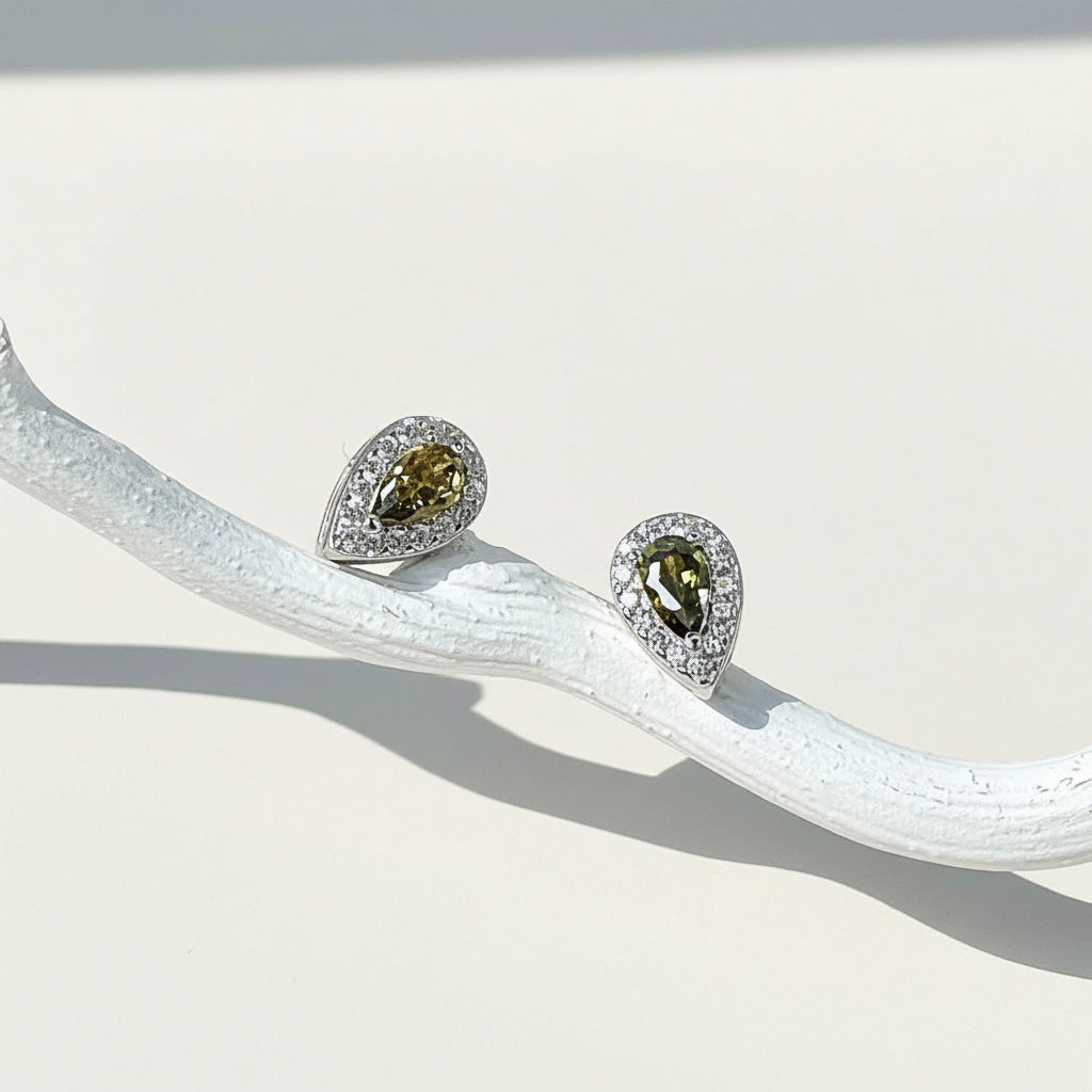 Teardrop stud earrings with olive green birthstone, platinum-plated silver setting, and halo of clear cubic zirconia.