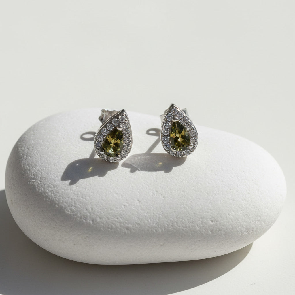 Teardrop silver stud earrings with platinum plating, green birthstone center, and halo of clear cubic zirconia.