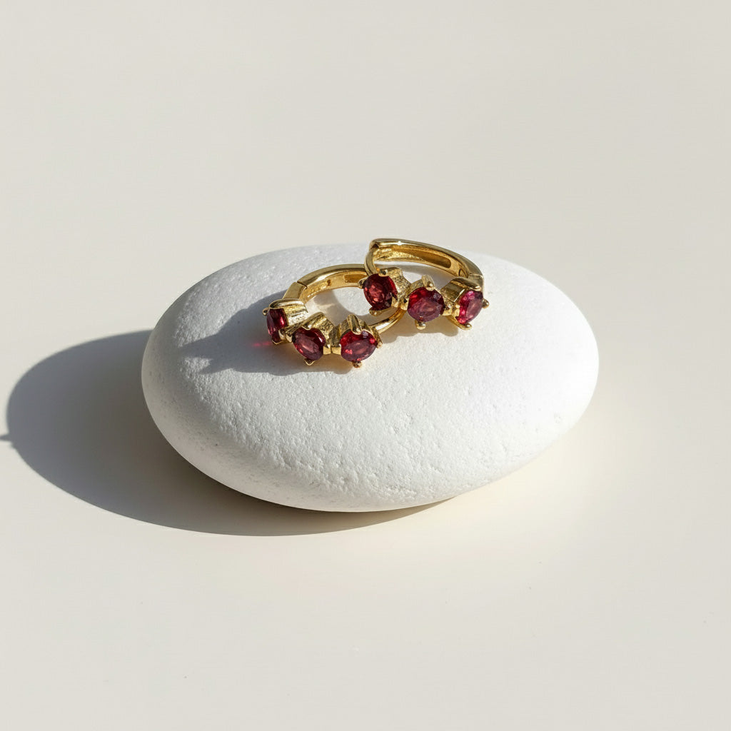 Gold-plated silver hoop earrings with red CZ birthstones, elegant minimalist design by A2K London.
