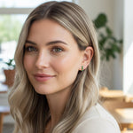 Woman wearing gold-plated silver hoop earrings with green cubic zirconia birthstones, minimalist May birthstone style.