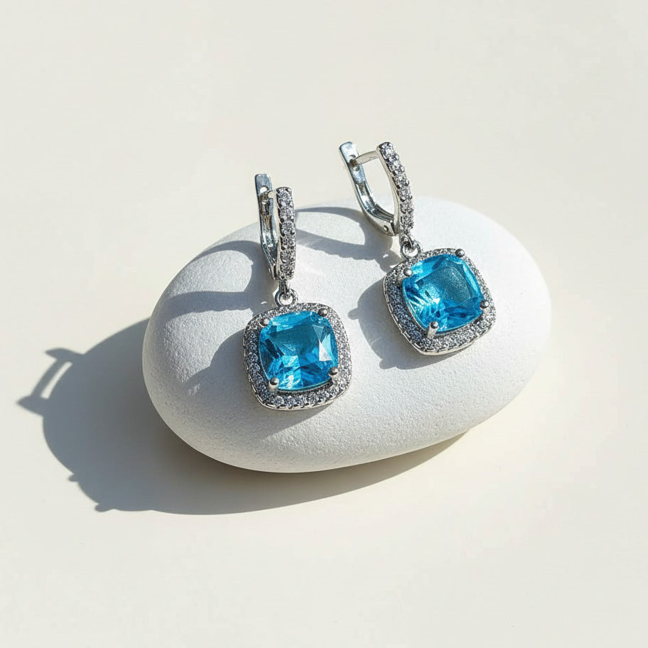 Blue topaz birthstone dangle earrings with cushion-cut stone and halo CZ, platinum-plated silver leverback design.