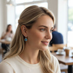 Model wearing blue topaz birthstone dangle earrings with cushion-cut stone and halo CZ, platinum-plated silver design.