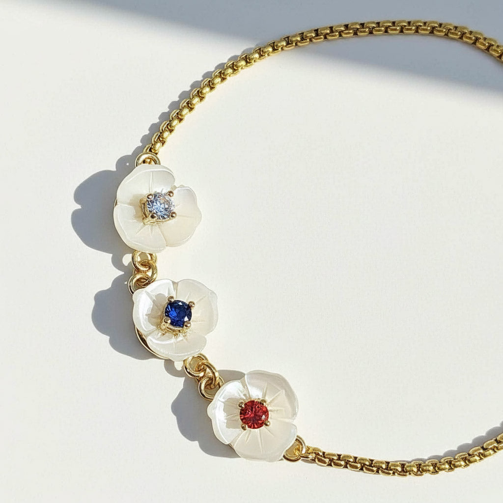 Gold bracelet with three mother-of-pearl flower charms featuring red, blue, and clear cubic zirconia birthstones.