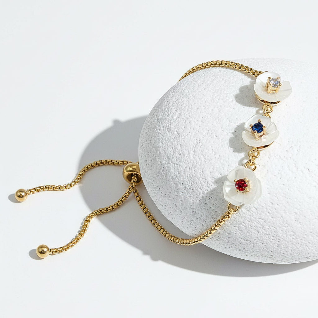 Gold adjustable bracelet with three white mother-of-pearl flower charms featuring red, blue, and clear birthstones.
