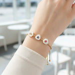 Model wearing gold adjustable bracelet with three white flower charms featuring red, blue, and clear birthstones.