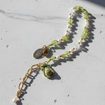 Necklace with green pendant and gold chain on a light gray surface