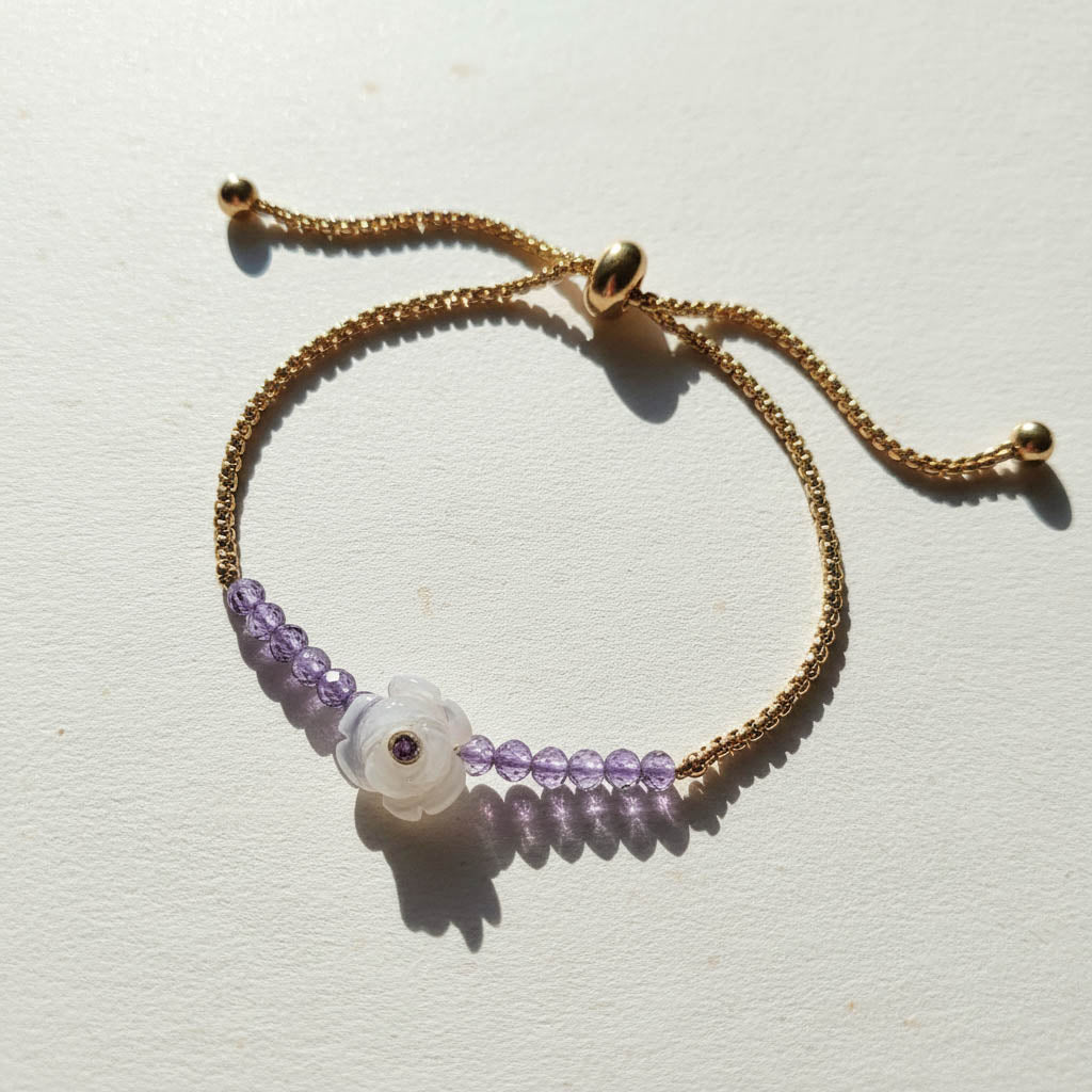 Gold adjustable bracelet with amethyst beads and carved white flower charm featuring a purple gemstone centre.
