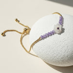 Gold adjustable bracelet with purple beads and white carved flower centrepiece featuring a small amethyst gem