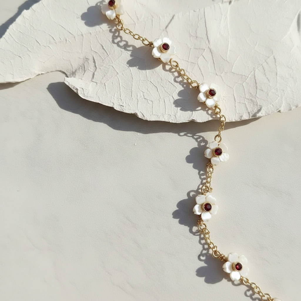 Gold chain necklace with white floral pendants on a textured beige surface