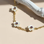 Gold bracelet with white floral charms and purple stones on a beige background