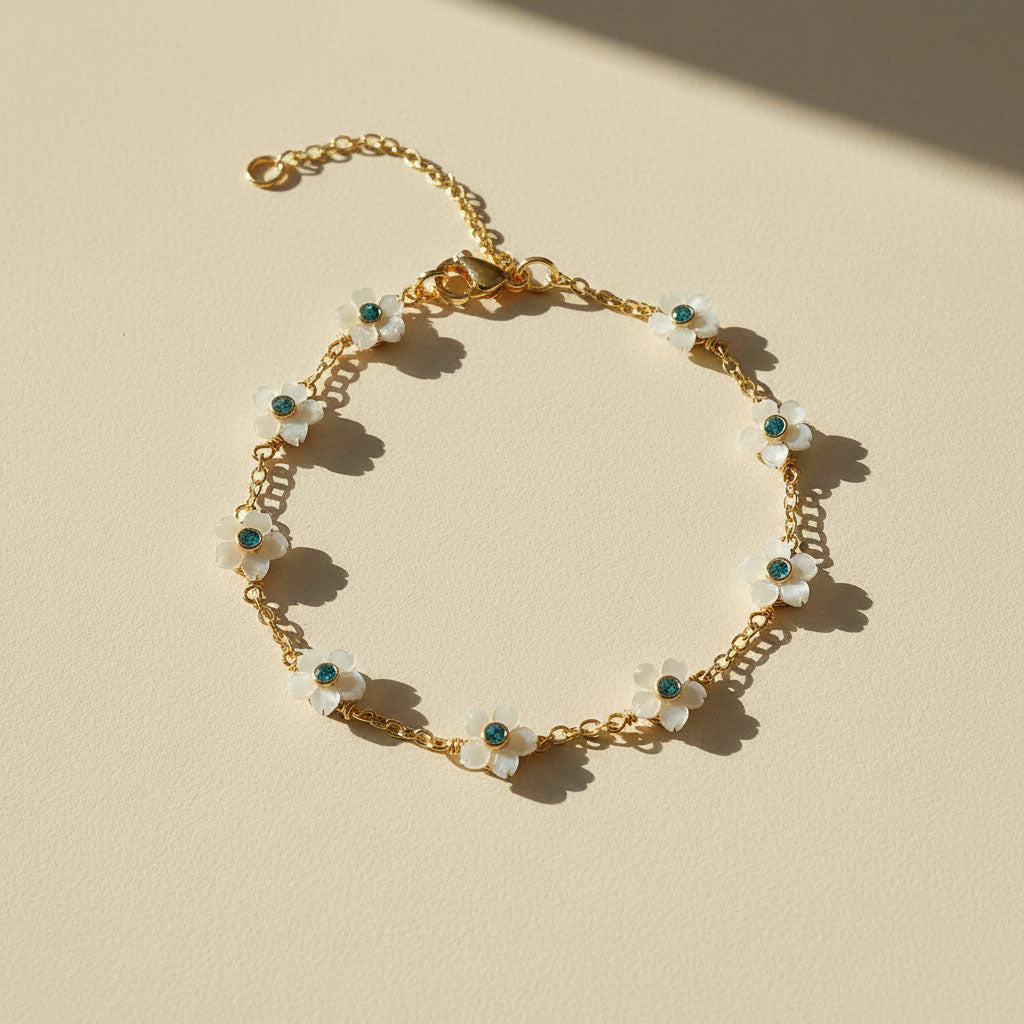 Gold bracelet with white floral charms on a beige background