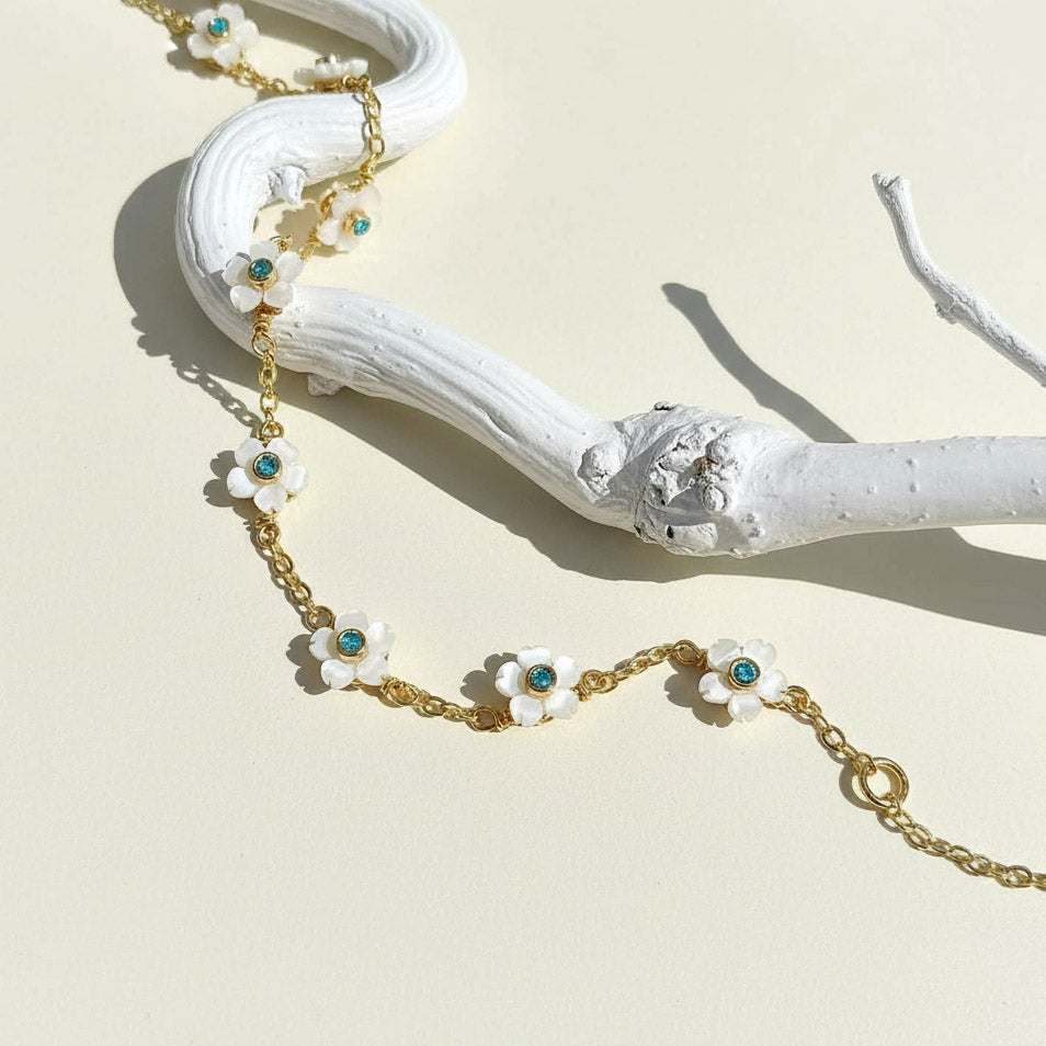 Gold chain necklace with floral pendants on a white branch