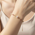 Gold bracelet with floral charm on a wrist against a neutral background