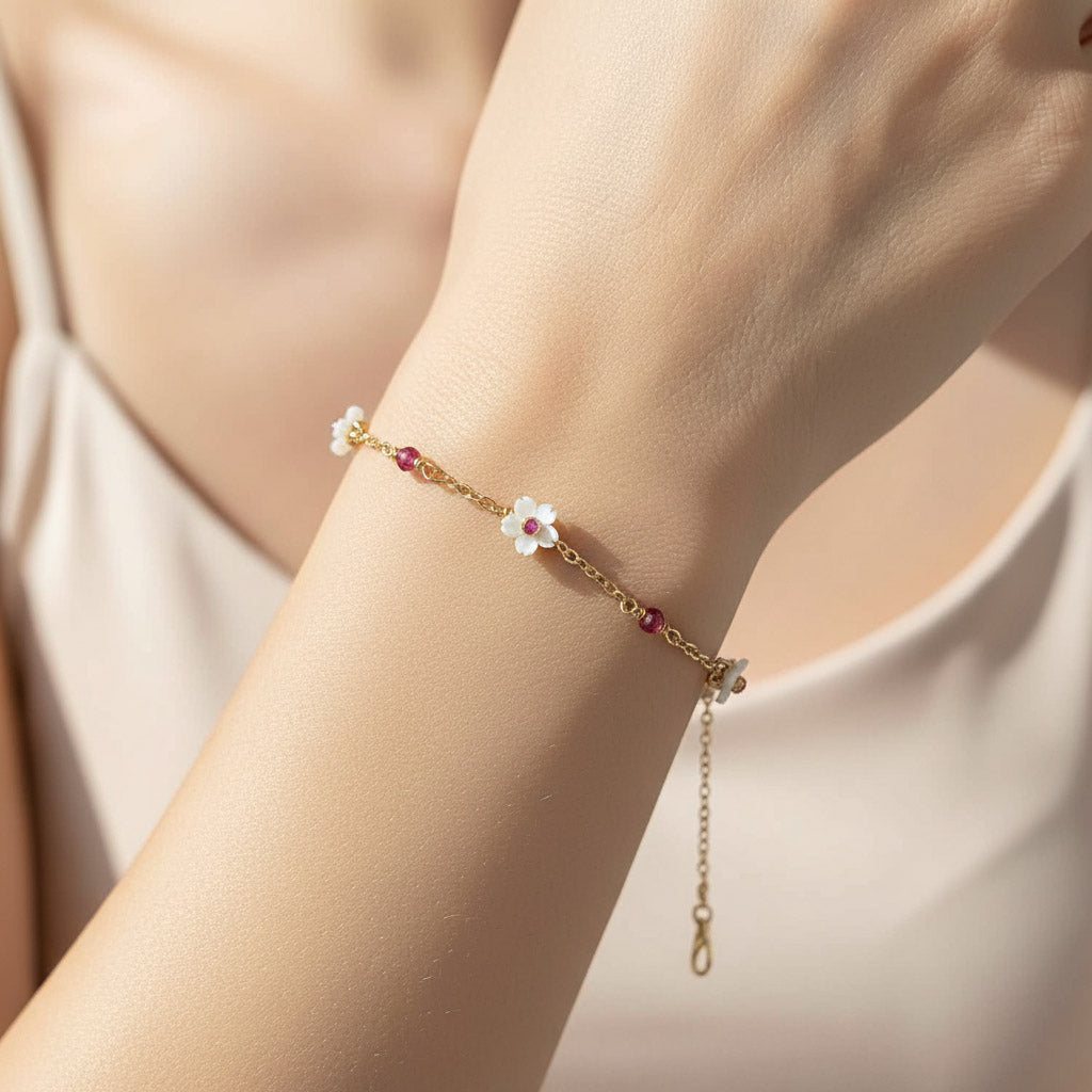 Gold bracelet with floral charm on a wrist against a neutral background