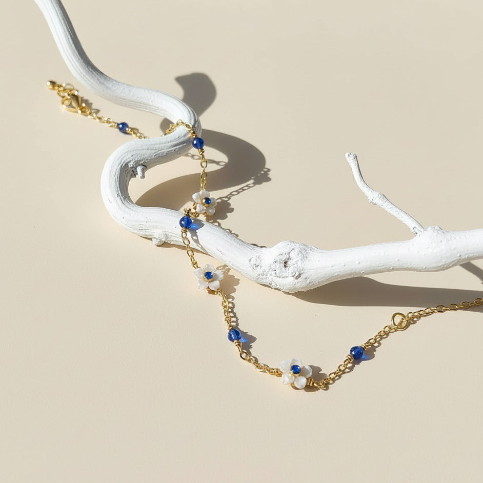 Gold necklace with blue and white beads on a white branch against a beige background