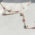 Delicate gold chain necklace with pink beads and white floral pendants on a light background