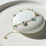 Gold bracelet with green beads on a white stand