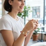 Woman holding a cup with a bracelet on her wrist, sitting indoors.
