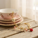 Bracelet with floral and strawberry charms on a wooden surface with a tea set in the background