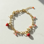 Gold bracelet with strawberry and flower charms on a light background