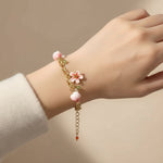 Hand wearing a delicate bracelet with pink beads and floral elements on a beige background