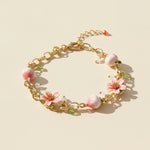 Gold bracelet with pink floral charms on a beige background