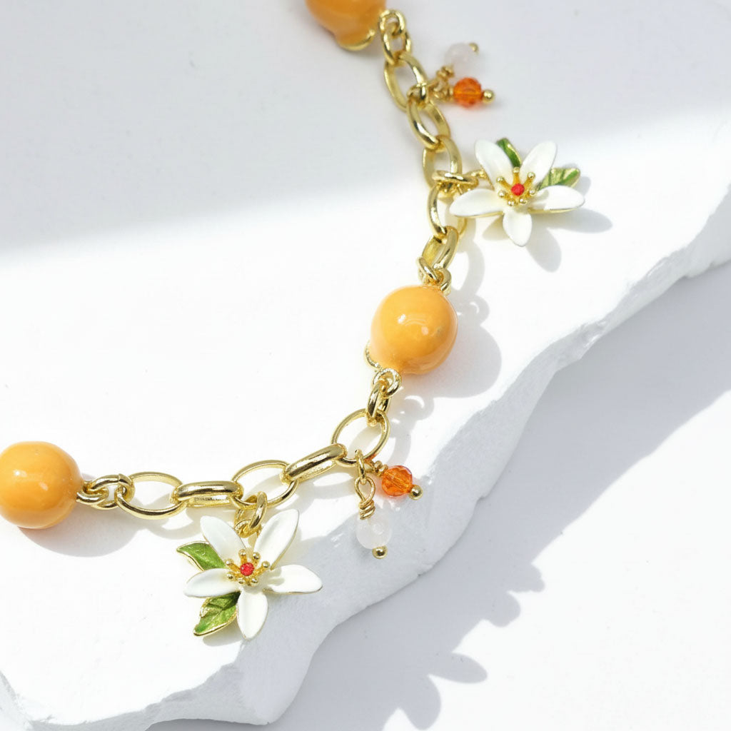 Bracelet with gold chain, orange beads, and white floral charms on a white background